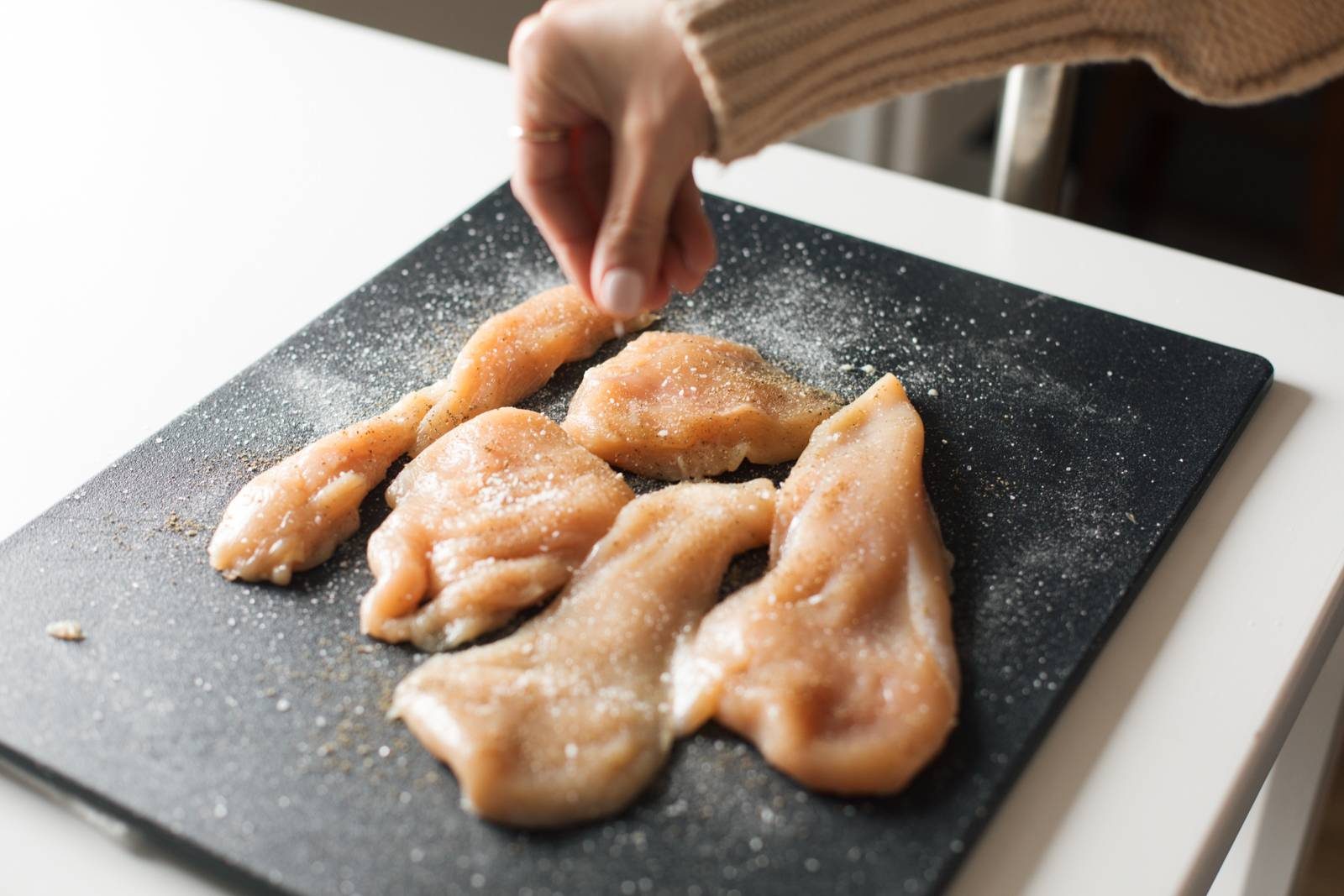 Raw thinly sliced chicken on a cutting board. 