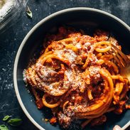 Bucatini in a bowl with red sauce and pecorino on top.